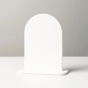 Op de afbeelding: Een witte displaystandaard met een boogvormige bovenkant. De standaard heeft een rechthoekige basis en een afgeronde bovenkant, wat een minimalistisch ontwerp creëert. Gemaakt van een solide, ondoorzichtig materiaal.