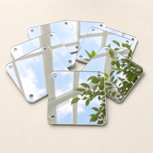 Peut inclure: Un ensemble de carreaux de miroir carrés et réfléchissants disposés en groupe. Chaque carreau individuel présente une surface lisse argentée et comprend quatre petits trous circulaires pré-percés situés près de chaque coin pour la fixation.