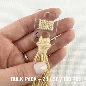Op de afbeelding: Een doorzichtige flosskaart met een klein gestikt voorbeeld en het nummer 945. De kaart is bevestigd aan een bundel beige draad. De tekst "BULK PACK - 20 / 50 / 100 PCS" is onderaan zichtbaar.