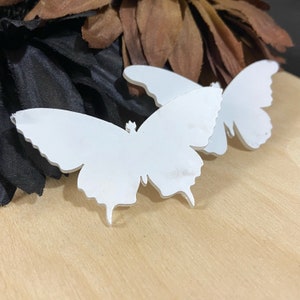 May include: Two white butterfly shaped acrylic decorations. The butterflies are cut out and have a smooth, glossy finish.