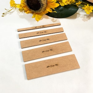 May include: Five wooden craft blanks with a brown finish. Each blank has a different measurement printed on it: 1 inch, 2 inches, 3 inches, 4 inches, and 5 inches.