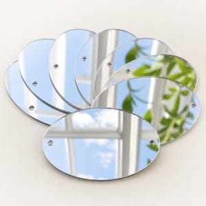 May include: A set of seven oval-shaped silver-toned mirrors arranged in a fan pattern. Each individual mirror features a smooth, reflective surface and two small, circular holes positioned on opposite sides for mounting or attachment purposes.