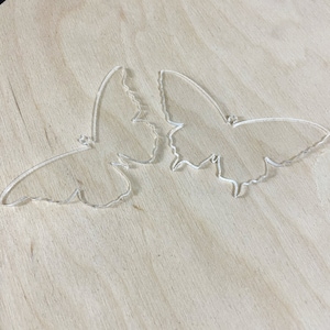 May include: Two clear acrylic butterfly shapes on a light brown wooden surface.
