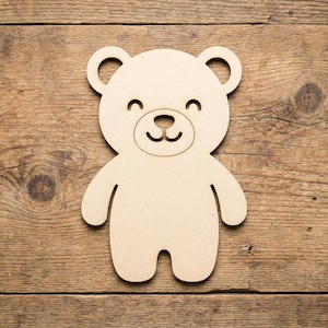 Könnte beinhalten: Aus Holz gefertigte, hellbraune Bär-Form mit einem lächelnden Gesicht. Der Bär hat ein einfaches Design mit abgerundeten Ohren, einer kleinen Nase und einem gebogenen Mund. Auf einer Holzoberfläche platziert.