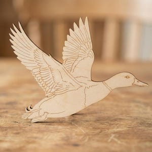 May include: A wooden duck in flight, with detailed wing and feather carvings. The duck is light brown and appears to be made of plywood. The duck is a decorative item, possibly for home decor or a craft project.