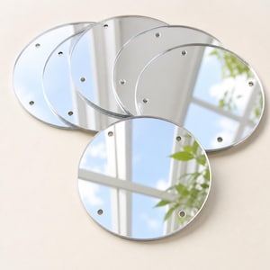 Op de afbeelding: Een set van vijf ronde, zilverkleurige spiegels, elk voorzien van vier kleine, gelijkmatig verdeelde, voorgeboorde gaten langs de rand. De reflecterende oppervlakken tonen een helder beeld van een raamkozijn en groen gebladerte.