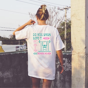 Könnte beinhalten: Weißes T-Shirt mit einem grafischen Design auf der Rückseite. Das Design enthält den Text "DO YOU EVEN LIFT?" über einer Gewichtheber-Illustration und die Worte "NO PAIN, NO GAIN". Das Shirt hat eine lässige, übergroße Passform.