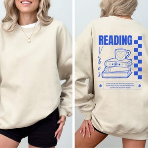 a woman wearing a sweatshirt that reads reading with a stack of books on it