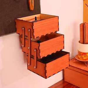 Könnte beinhalten: Ein Satz aus drei Holzkisten mit einer natürlichen Holzoptik. Die Kisten sind vertikal gestapelt und an einer Wand befestigt. Die Kisten sind aus Sperrholz und haben ein schlichtes Design.