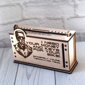 May include: Wooden box with a cutout of the Terminator character and the text "I need your money and keys for your bike! Sincerely yours, Terminator T800."
