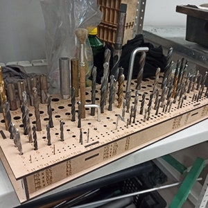 Op de afbeelding: Een houten boorhouder met een verscheidenheid aan boren en een borstel. De houder is gelabeld met de maten van de boren, waaronder M3 x 0,5, M4 x 0,7, M5 x 0,8 en M6 x 10.