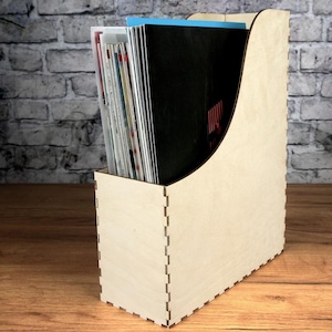 May include: A wooden magazine holder with a curved front and a natural wood finish. The holder is filled with magazines and books.