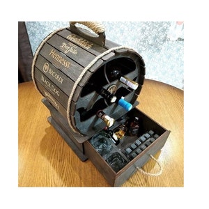 Könnte beinhalten: Ein hölzerner Likörschrank in Fassform mit einer Schublade. Der Schrank hat einen Seilgriff und ist mit den Namen verschiedener Likörmarken verziert, darunter Glenfiddich, Don Julio, Hennessy, Bacardi und Black Dog. Die Schublade ist geöffnet und enthält Gläser und Eiswürfel.