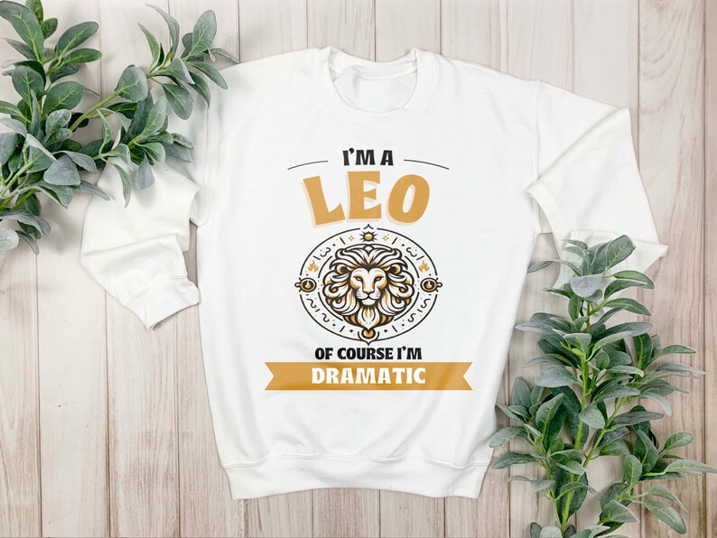May include: White long-sleeved sweatshirt with a gold graphic of a lion and the text "I'm a Leo Of course I'm Dramatic".