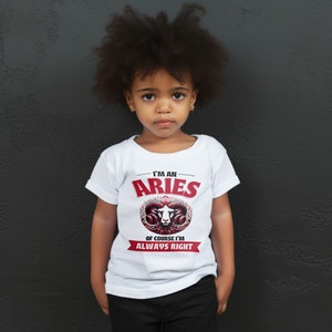 May include: A young person wearing a white t-shirt with a red and black graphic of a ram's head and the text "I'm an Aries. Of course I'm always right."
