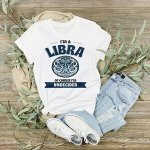 May include: White t-shirt with a blue Libra zodiac symbol and the text "I'm a Libra, of course I'm undecided."