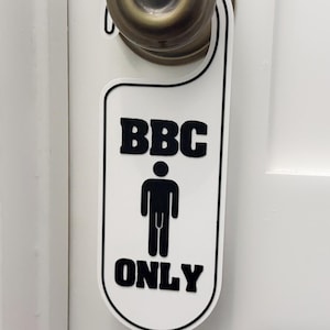 May include: A white door hanger with a black border and black text that reads BBC ONLY, featuring a black graphic icon of a person in the center, hanging from a round, metallic, bronze-colored door knob on a white paneled door.