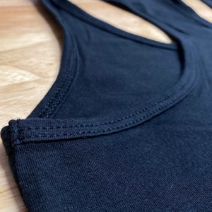 May include: Close-up of the neckline of a black tank top with a double-stitched seam.