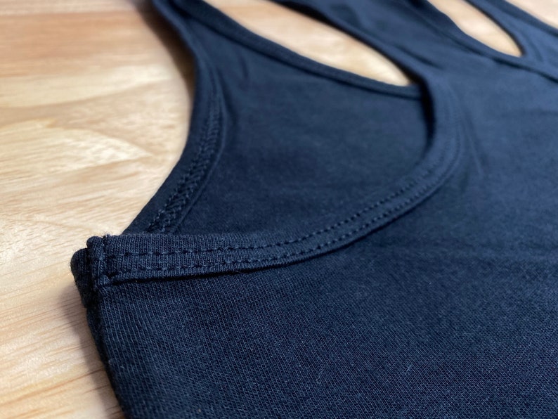 May include: Close-up of the neckline of a black tank top with a double-stitched seam.