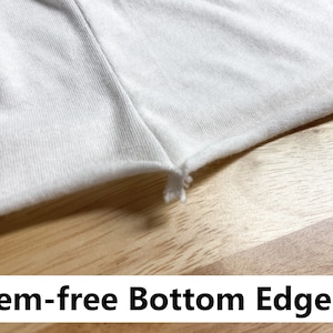 May include: Close-up of a white fabric with a raw, unfinished edge. The fabric is smooth and has a slight sheen. The edge is frayed and uneven. The fabric is lying on a wooden surface. Hem-free bottom edge.