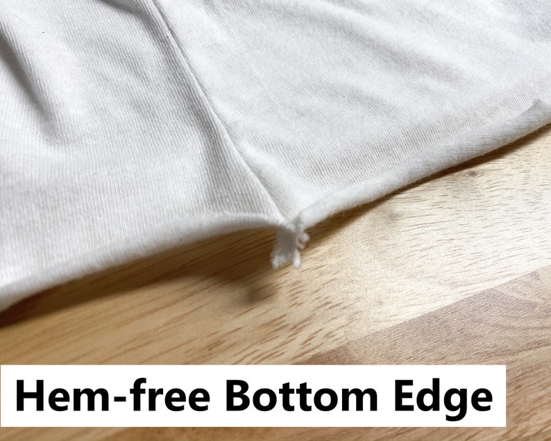 May include: Close-up of a white fabric with a raw, unfinished edge. The fabric is smooth and has a slight sheen. The edge is frayed and uneven. The fabric is lying on a wooden surface. Hem-free bottom edge.