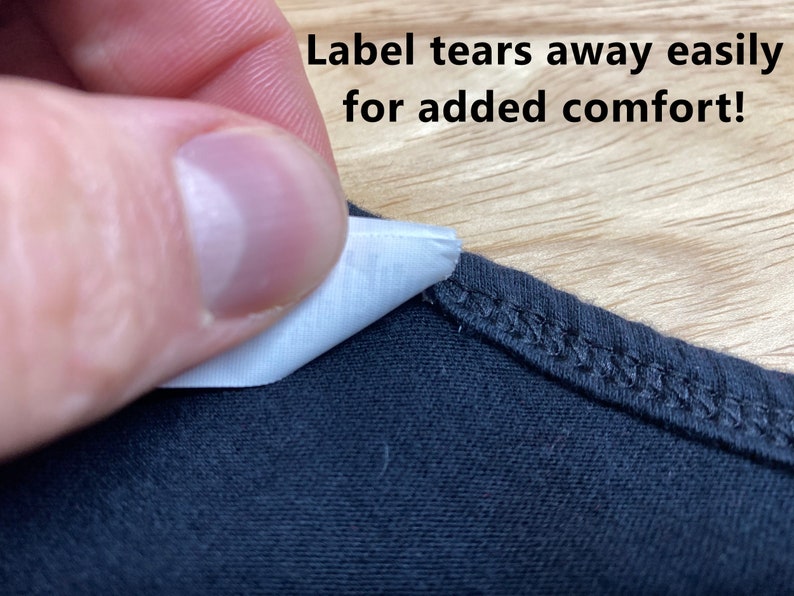 May include: A close-up of a black t-shirt with a white tag that says "Label tears away easily for added comfort!"