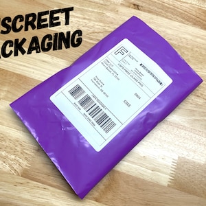 May include: A purple padded envelope with a white shipping label. The label has the text "USPS First Class PKG" and a tracking number. The envelope is on a wooden surface.