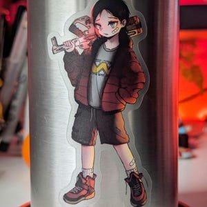 May include: A sticker of a cartoon character with short black hair, wearing a red jacket, blue jeans, and black boots. The character is holding a large, silver weapon with a red handle. The sticker is on a silver water bottle.