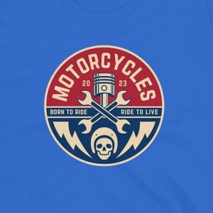 May include: A blue t-shirt with a red, white, and blue circular graphic. The graphic features a skull wearing a helmet, crossed wrenches, and a piston. The text "Motorcycles" is written in a circular arc above the graphic. The text "Born to Ride" is written below the graphic on the left, and the text "Ride to Live" is written below the graphic on the right.