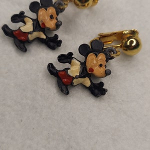 May include: A pair of vintage Mickey Mouse clip-on earrings. Each earring features a running Mickey Mouse figure in black, red, and tan. The clip-on mechanism is gold-toned.