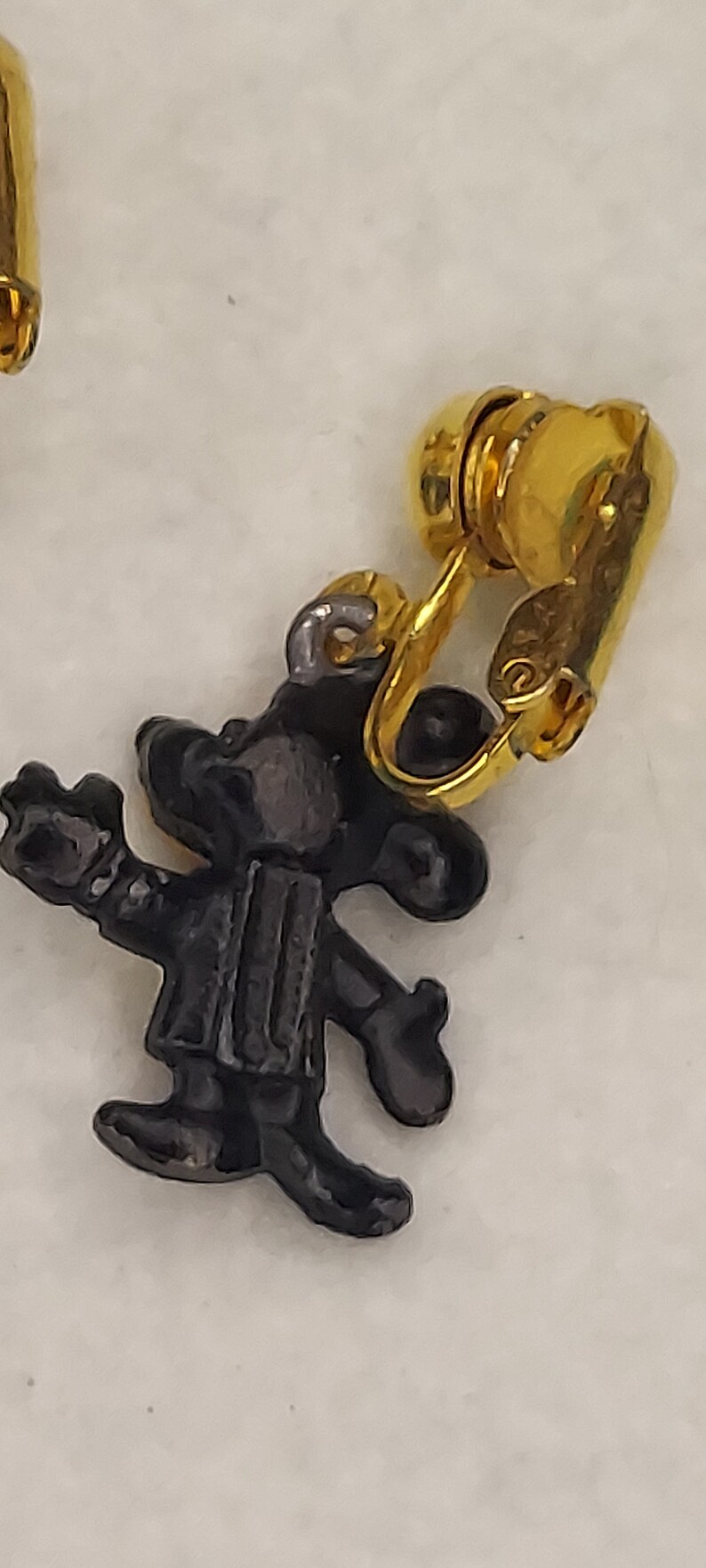 May include: A vintage clip-on earring featuring a black cartoon character with a gold-tone clip. The character is wearing a vest and hat. The earring is set against a white background.