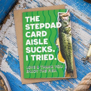 May include: A greeting card with a green background and the text "THE STEPDAD CARD AISLE SUCKS. I TRIED. LOVE & THANK YOU ENJOY THE FISH." A fish illustration is on the right side. The card is on a brown envelope.