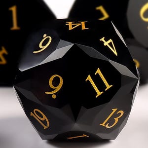 May include: Close-up of several black polyhedral dice with gold numbering. The dice have a faceted design and are set against a white background. The numbers are clearly visible, with a focus on the larger dice.