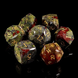 May include: A set of seven polyhedral dice, featuring a mix of green and red hues with gold numbering. The dice are designed for tabletop role-playing games, with various shapes including a d20, d12, d10, d8, d6, and d4.