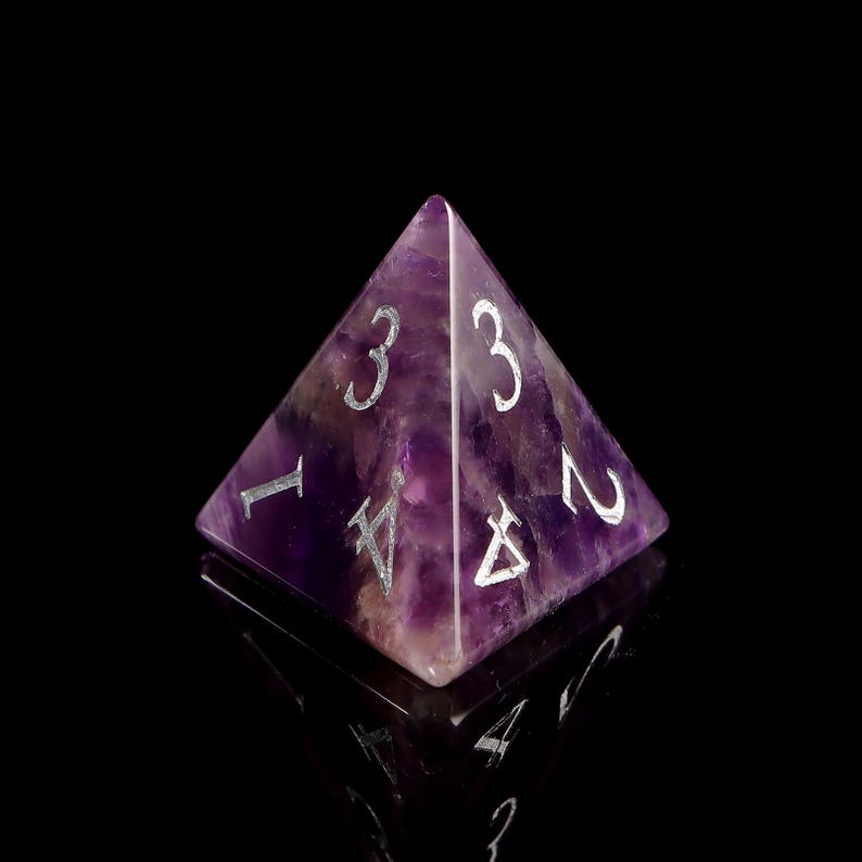 May include: A purple amethyst pyramid-shaped dice with silver numbers 1, 2, 3, and 4.