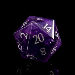 May include: A purple 20-sided die made of amethyst with silver numbers. The die is showing the number 20.