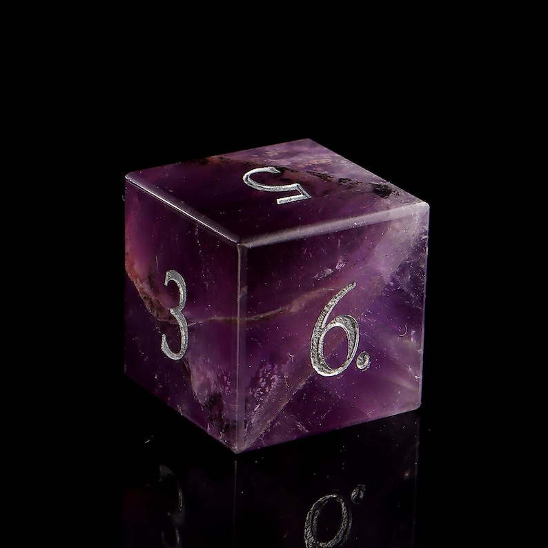 May include: A purple amethyst gemstone dice with the numbers 3, 6, and 9 engraved on the visible sides.