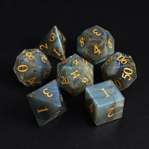 May include: Set of seven blue and green gemstone dice with gold numbers. The dice are numbered 1 through 6, 4, 9, 14, 20, 50.