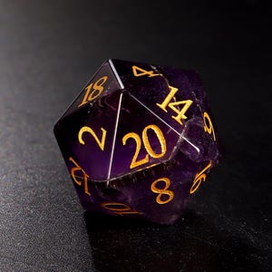 May include: A purple 20-sided die with gold numbers. The die is made of natural stone and has a unique, textured surface.