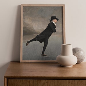 May include: A framed print of a man in a black coat and top hat ice skating on a frozen lake. The background is a blurry landscape with mountains in the distance.