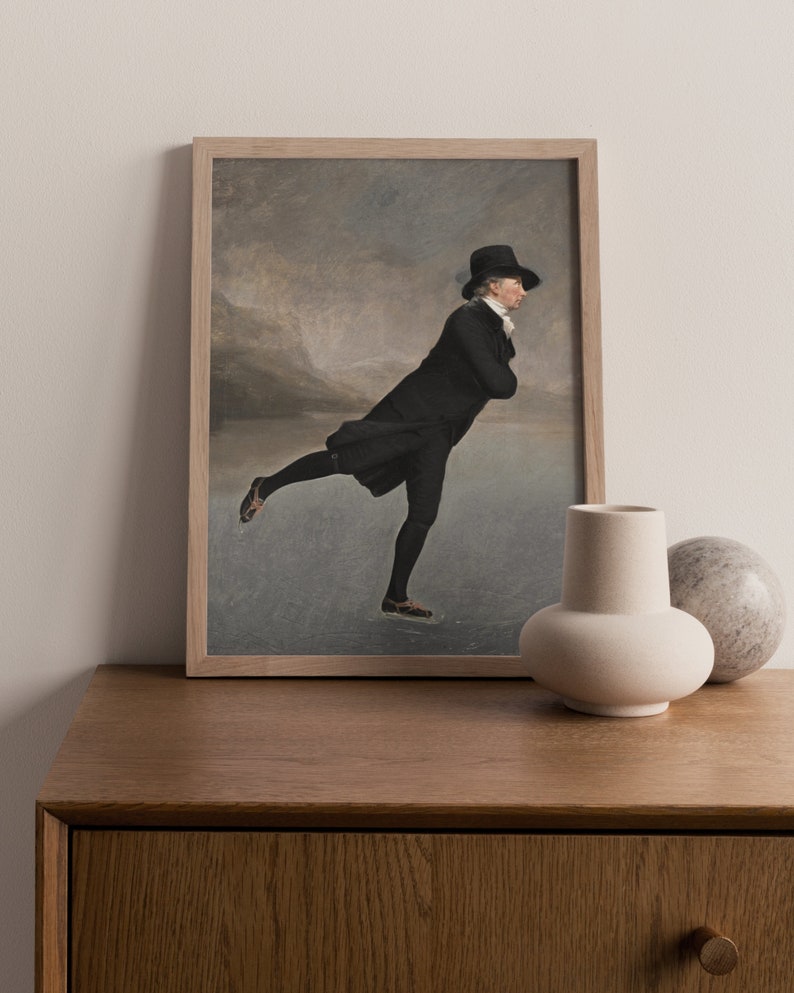 May include: A framed print of a man in a black coat and top hat ice skating on a frozen lake. The background is a blurry landscape with mountains in the distance.