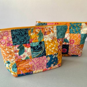 May include: Two quilted zippered pouches with a patchwork design featuring a variety of floral and paisley patterns in shades of orange, pink, teal, and yellow.