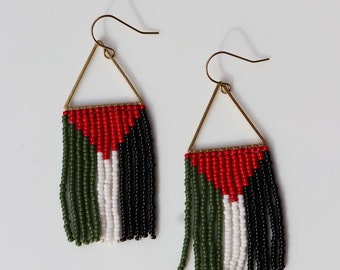 May include: A pair of gold triangle dangle earrings with green, white, and red beaded fringe. The beads are arranged in a pattern that resembles a flag.