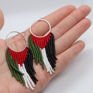 Puede incluir: Un par de pendientes de aro con flecos de cuentas en los colores de la bandera de los Emiratos Árabes Unidos: verde, blanco, negro y rojo.