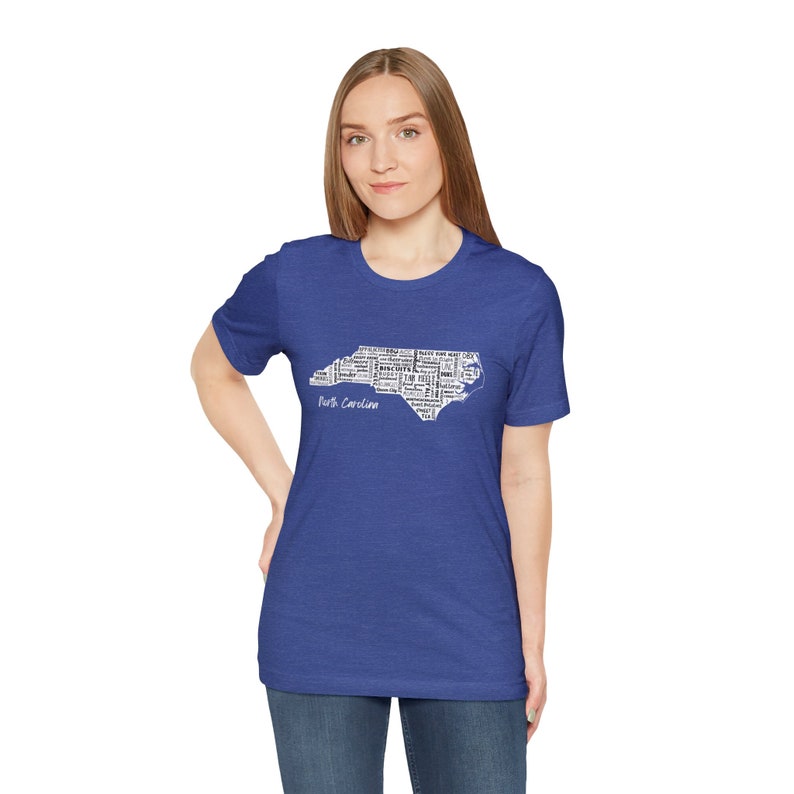 Pu&ograve; includere: Una t-shirt blu reale con un contorno bianco dello stato della Carolina del Nord pieno di testo. Il testo include citt&agrave;, monumenti e altre cose associate allo stato. Il testo recita "Carolina del Nord".