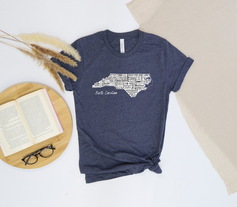 Pu&ograve; includere: Una maglietta blu navy con un contorno bianco dello stato della Carolina del Nord. Il contorno &egrave; composto da parole relative allo stato, come citt&agrave;, monumenti e altri punti di interesse. Le parole "Carolina del Nord" sono stampate sotto il contorno.