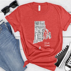 K&ouml;nnte beinhalten: Rotes T-Shirt mit einer wei&szlig;en Umrandung des Bundesstaates Rhode Island, gef&uuml;llt mit Text, der sich auf den Bundesstaat bezieht. Der Text enth&auml;lt "Rhode Island", "The Ocean State", "Coffee Milk", "Waterfire", "Doughboys", "Brown University", "Bryant Bulldogs", "Narragansett Bay", "Roger Williams", "V-J Day", "101 Grinders", "Smallest State", "Lobsters", "Cabinets", "Pizza", "Grams", "Yawgoo", "Tennis Hall of Fame", "South County", "Coastline" und mehr.