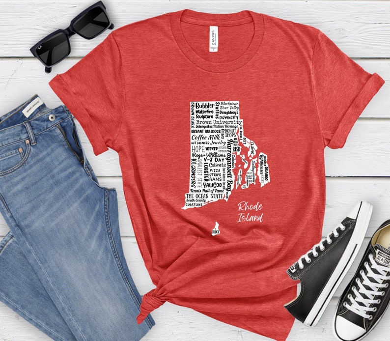 K&ouml;nnte beinhalten: Rotes T-Shirt mit einer wei&szlig;en Umrandung des Bundesstaates Rhode Island, gef&uuml;llt mit Text, der sich auf den Bundesstaat bezieht. Der Text enth&auml;lt "Rhode Island", "The Ocean State", "Coffee Milk", "Waterfire", "Doughboys", "Brown University", "Bryant Bulldogs", "Narragansett Bay", "Roger Williams", "V-J Day", "101 Grinders", "Smallest State", "Lobsters", "Cabinets", "Pizza", "Grams", "Yawgoo", "Tennis Hall of Fame", "South County", "Coastline" und mehr.