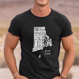 K&ouml;nnte beinhalten: Ein schwarzes T-Shirt mit einer wei&szlig;en Grafik des Bundesstaates Rhode Island. Die Grafik besteht aus W&ouml;rtern, die mit dem Bundesstaat in Verbindung stehen, wie "Coffee Milk", "Ocean State" und "Roger Williams".