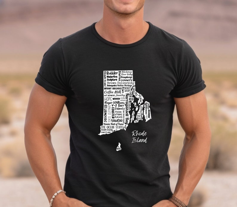 K&ouml;nnte beinhalten: Ein schwarzes T-Shirt mit einer wei&szlig;en Grafik des Bundesstaates Rhode Island. Die Grafik besteht aus W&ouml;rtern, die mit dem Bundesstaat in Verbindung stehen, wie "Coffee Milk", "Ocean State" und "Roger Williams".